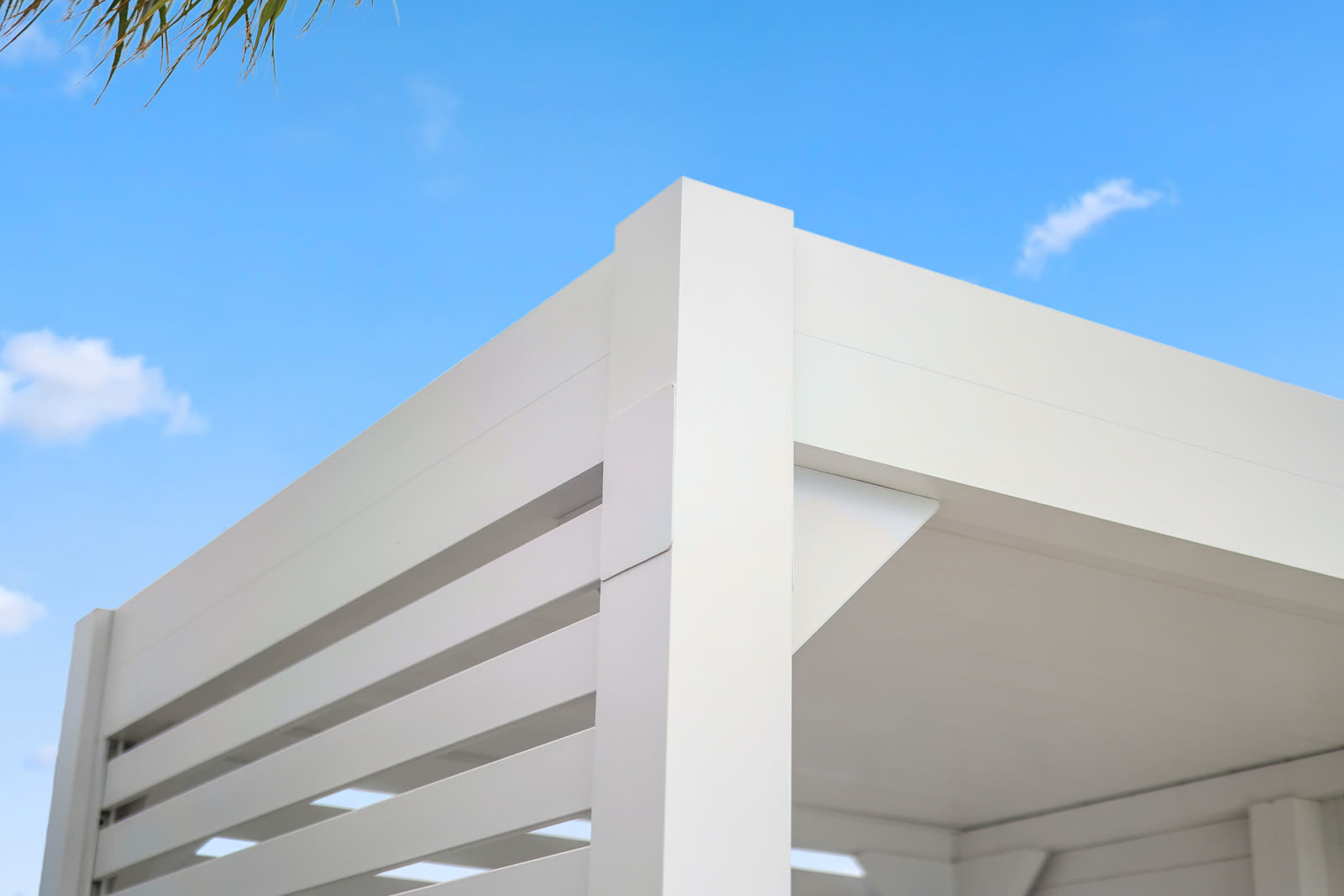 White Azenco R-BLADE louvers rotated toward closed position, blocking direct overhead sun while venting hot air upward at the peak of the louver stack.