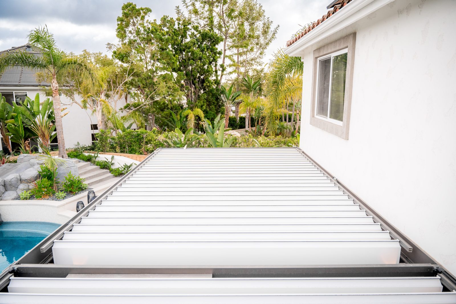 Dark gray R-BLADE pergola with fans and heaters beside a pool